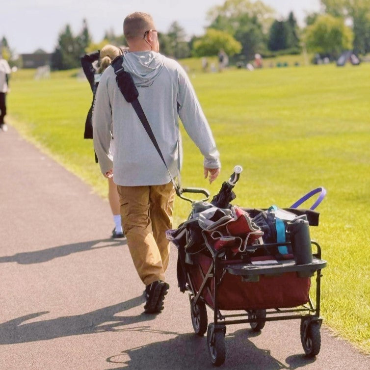 Man pushing a cart with belongings on a path in a park