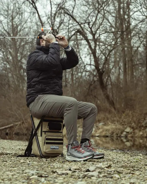 Adult sitting on a tan StoolPak while casting at a creek